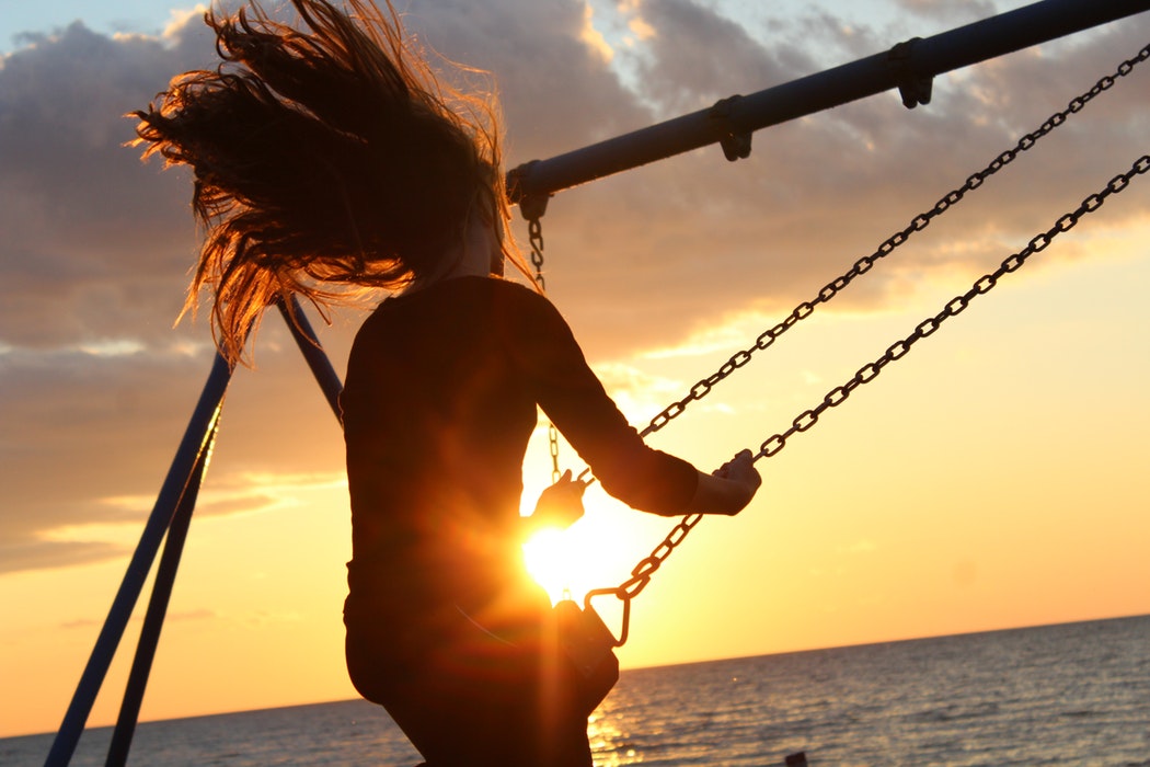 Woman on swing overlooking ocean during sunset