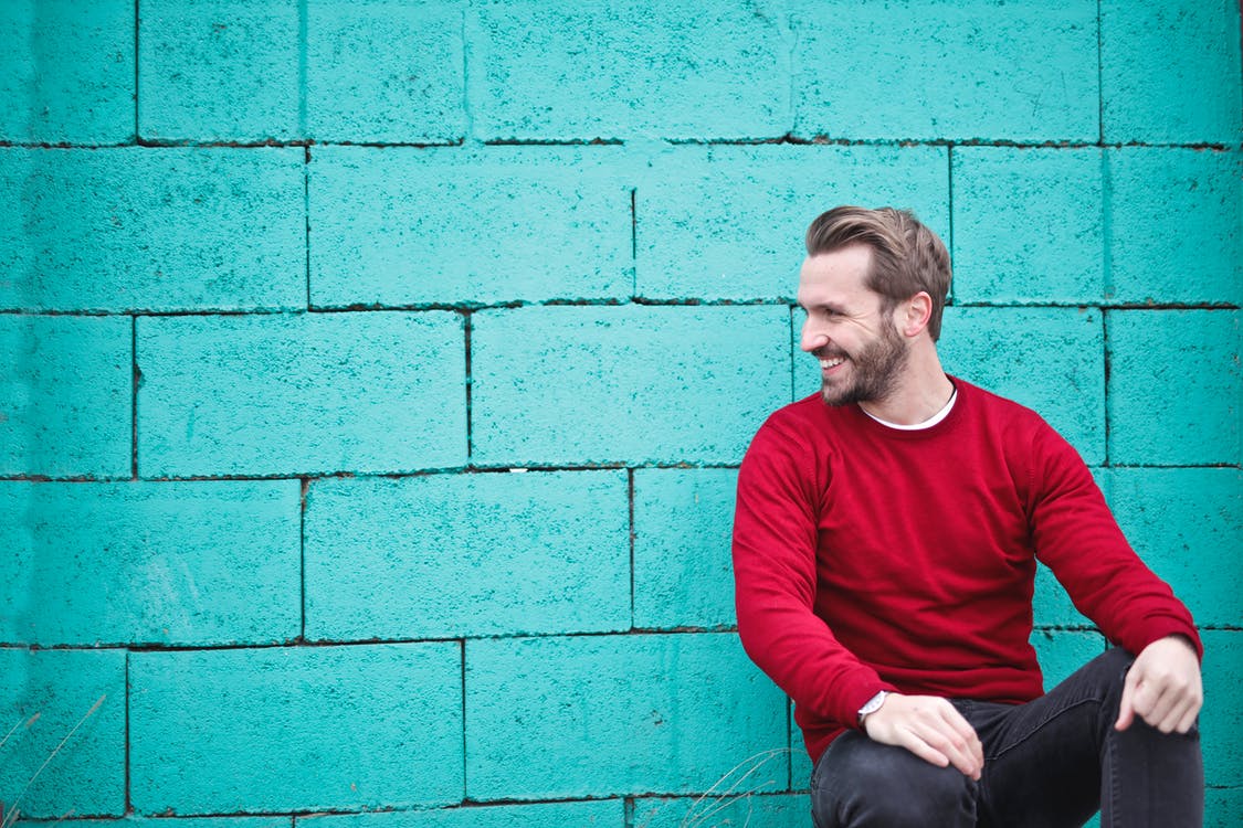 Man smiling in front of blue wall while looking off to his side