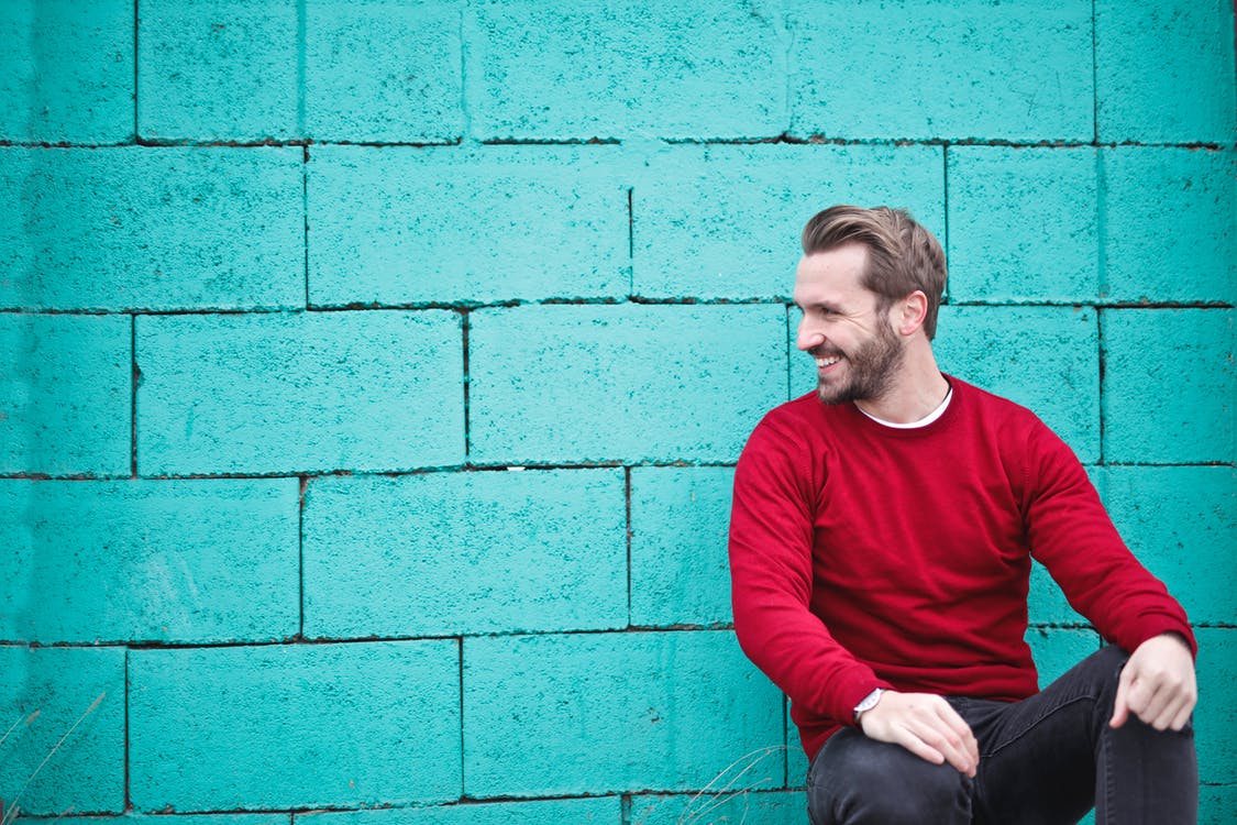 Man smiling in front of blue wall while looking off to his side