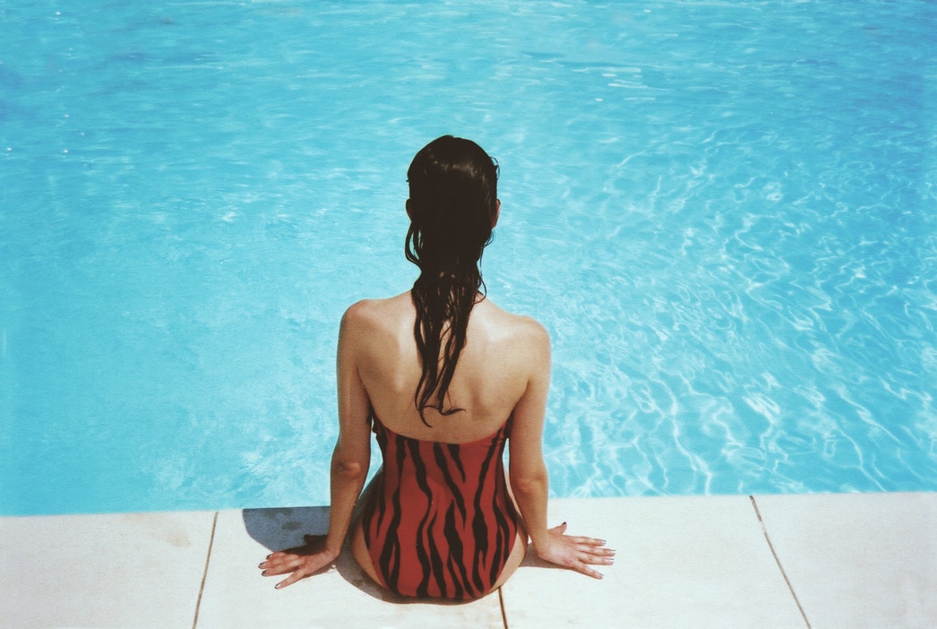 Woman in orange bathing suit sitting by pool