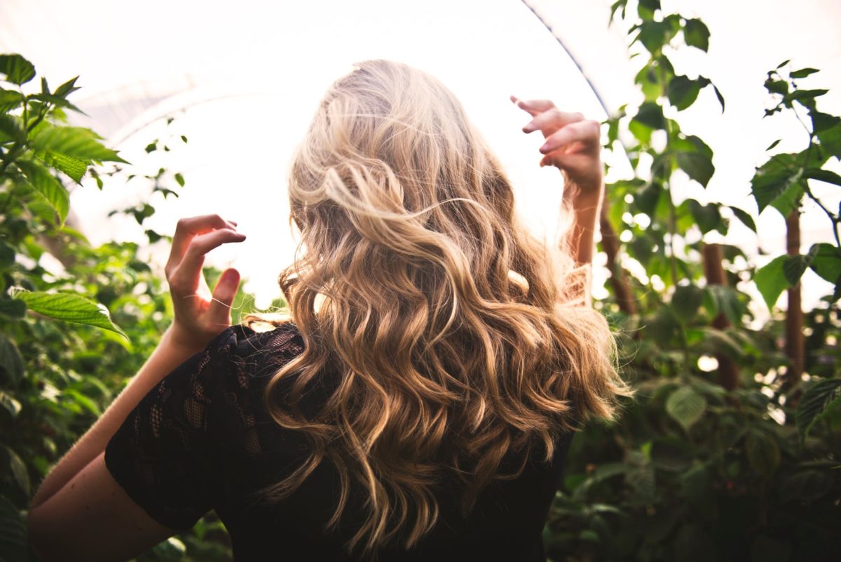 Woman with curly blonde hair walking through garden