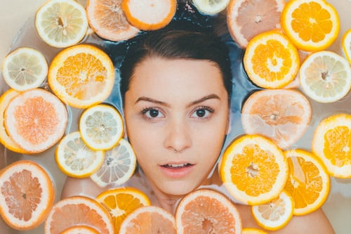Close up of woman's face in bathtub surrounded by floating orange and lemon peels