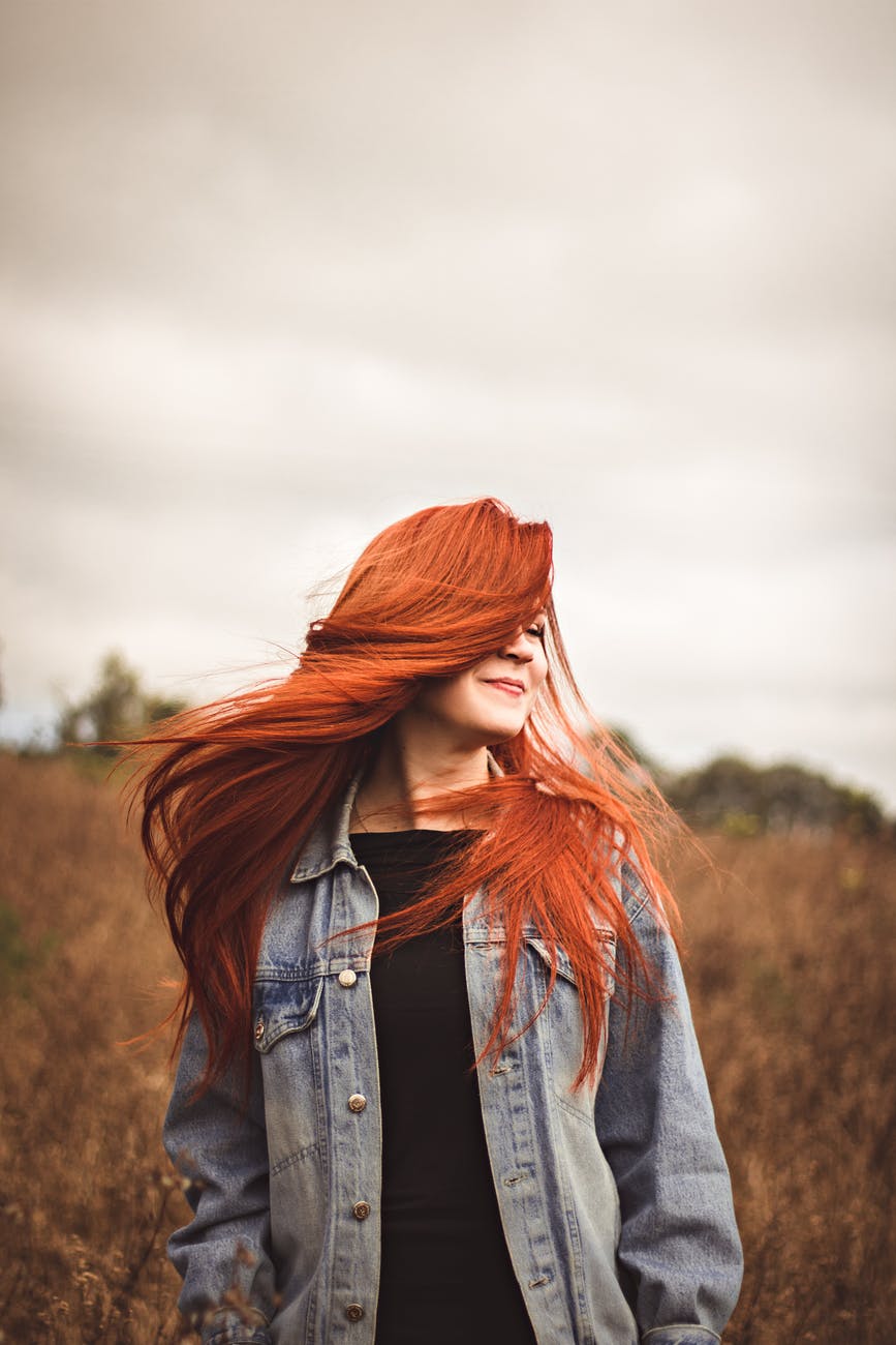 Red headed woman shakes her radiant hair in outdoor setting